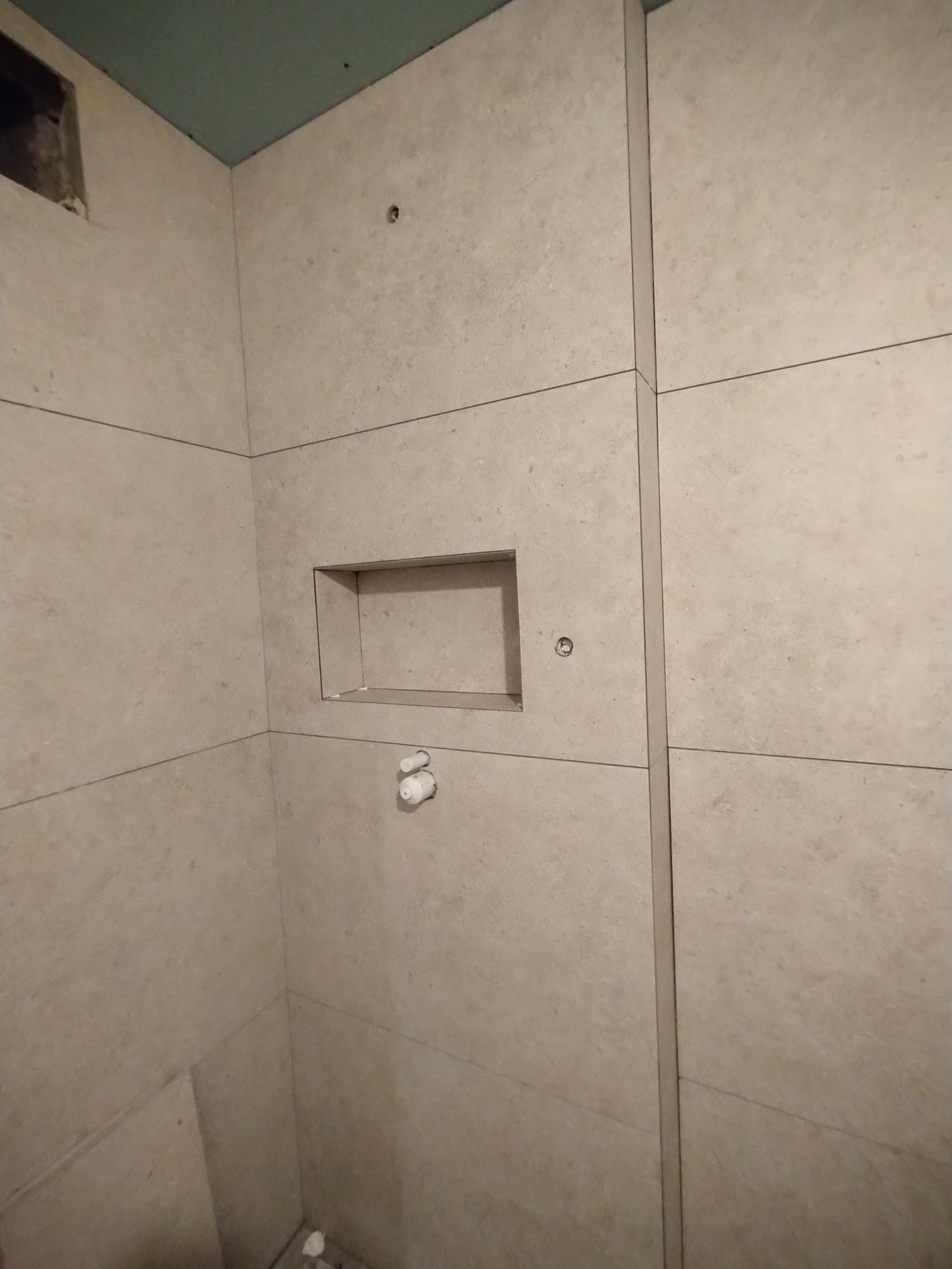 Wykończona łazienka z beżowymi płytkami, wnęką w ścianie i widocznymi elementami instalacji. Minimalistyczny design, świeżo po remoncie.