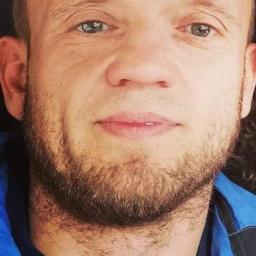 Firma remontowo wykonczeniowa Pras damian - Portret mężczyzny z krótkimi włosami i brodą, ubrany w niebieską kurtkę i granatowy sweter.