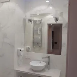 Nowoczesna łazienka z białą umywalką nablatową, chromowaną baterią, grzejnikiem drabinkowym i marmurowymi płytkami ściennymi.