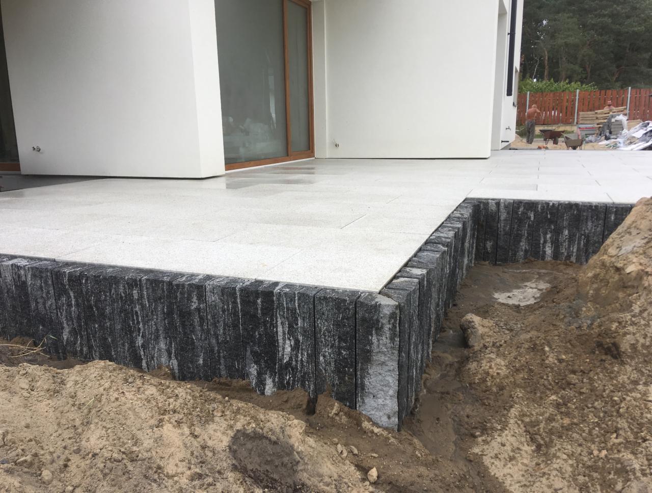 Jasnoszara, ułożona kostka na tarasie z obrzeżem z ciemnej kostki granitowej, widoczne prace ziemne w tle