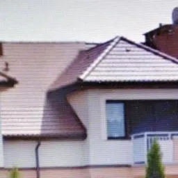 Panorama trzech segmentów bliźniaczych z dachami pokrytymi brązową dachówką, widoczne kominy, anteny satelitarne, rynny i fragmenty elewacji.