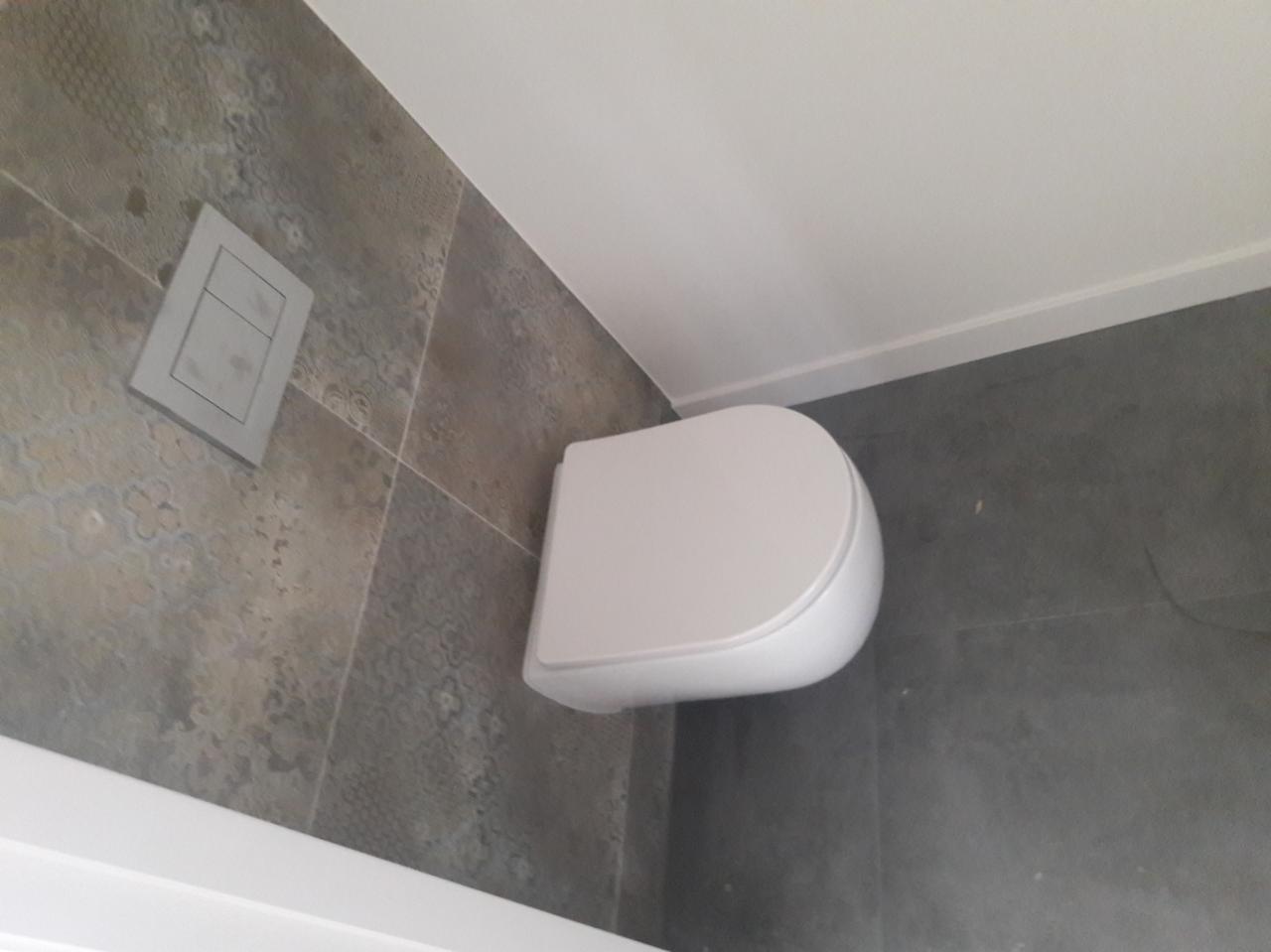 Nowoczesna toaleta podwieszana z szarą płytką dekoracyjną na ścianie i podłodze, widoczny przycisk spłukiwania.