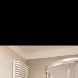 Nowoczesna kabina prysznicowa z chromowanymi elementami i grzejnik drabinkowy w wykończonej łazience z szarymi płytkami.