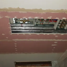 Sufit podwieszany z widoczną instalacją hydrauliczną i wentylacyjną w trakcie montażu, szpachlowane łączenia płyt gipsowych, widoczne przewody elektryczne wystające ze ściany.