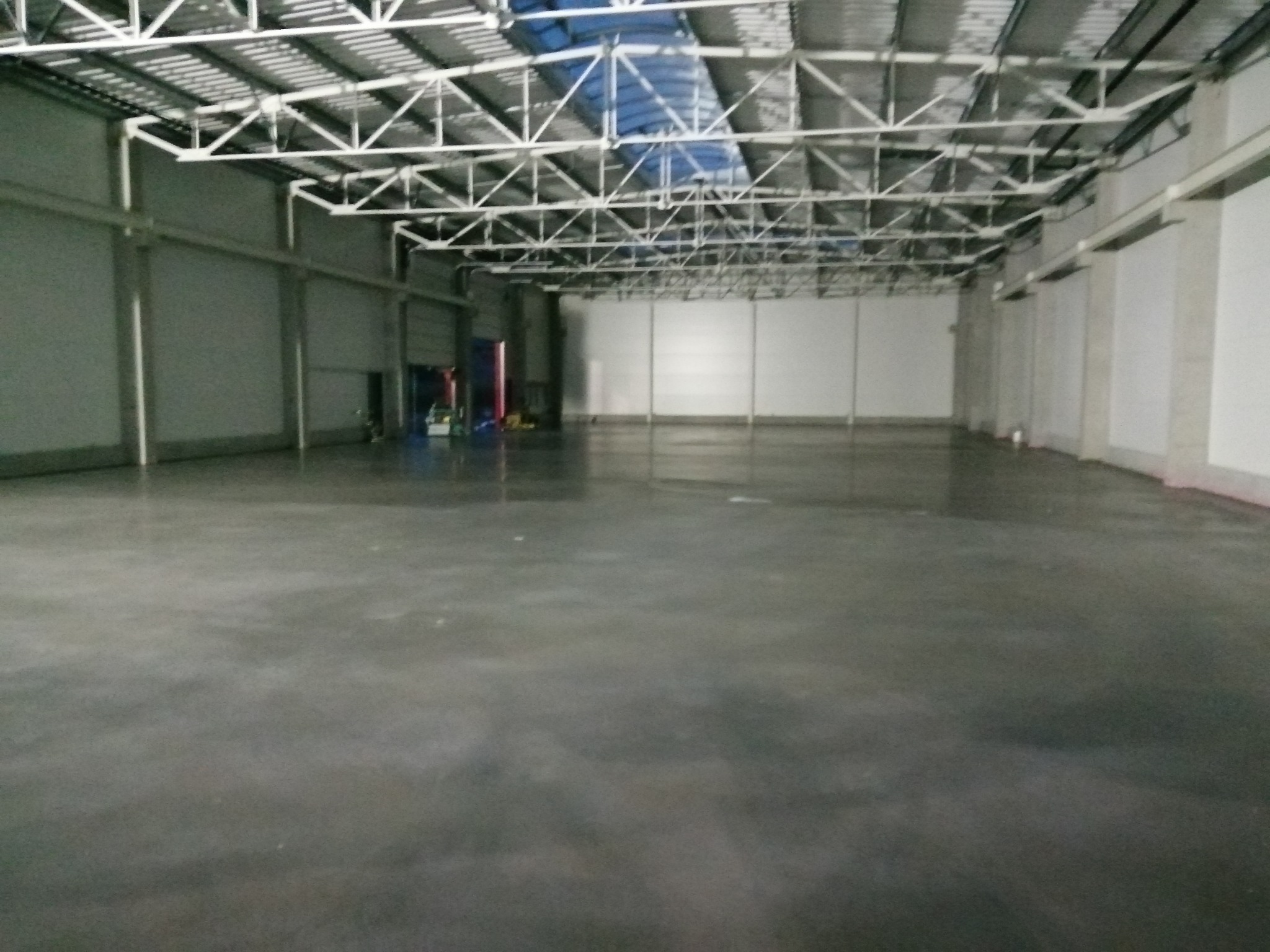 Gładka, szara posadzka w przestronnym, pustym magazynie z metalową konstrukcją dachu i jasnymi ścianami.