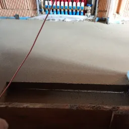 Świeżo wylana, szara posadzka z widocznymi elementami instalacji ogrzewania podłogowego i rozdzielaczem na ścianie w tle.