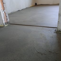 Posadzki Maszynowe Radosław Lisiecki - Świeżo wylana, gładka posadzka w pomieszczeniu z widocznymi fragmentami ścian i izolacją przy podłodze. Widoczna szczelina dylatacyjna.