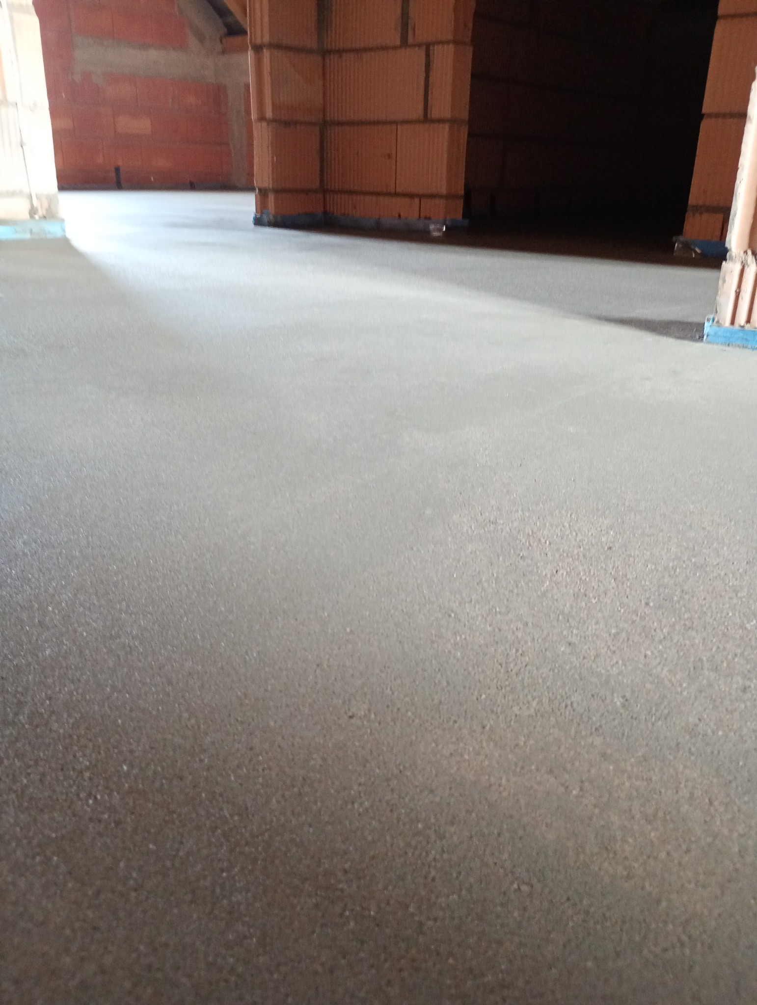 Świeżo wylana, gładka posadzka w surowym wnętrzu budynku z ceglanymi ścianami i słupami.