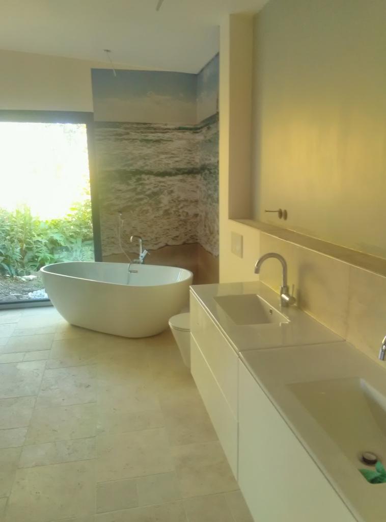 Nowoczesna łazienka z wolnostojącą wanną, podwójną umywalką w białej szafce i fototapetą z motywem morza na ścianie.