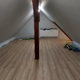 Poddasze po ułożeniu paneli podłogowych, widoczna drewniana belka konstrukcyjna, grzejnik i materiały budowlane w tle.