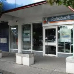 Fasada budynku banku Rabobank z czerwonymi filarami i szarym chodnikiem, widziana z zewnątrz.