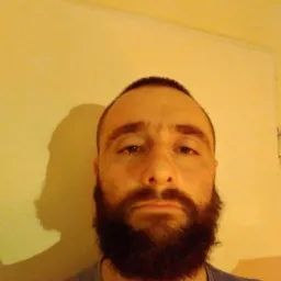 Portret brodatego mężczyzny na tle żółtej ściany z widocznym cieniem, ukazujący stan pomieszczenia przed potencjalnym odświeżeniem koloru.