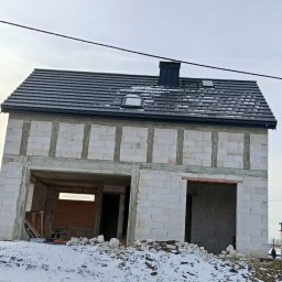 Usługi Remontowo Budowlane - Niedokończony, dwukondygnacyjny budynek z białych bloczków, z ciemnym dachem i kominem, w zimowym krajobrazie. Widoczne otwory okienne i drzwiowe, śnieg na dachu i ziemi.