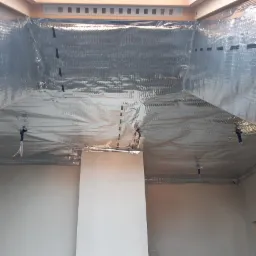 Wnętrze w trakcie ocieplania folią aluminiową, widoczne mocowania przewod&oacute;w i fragment drewnianej konstrukcji dachu.