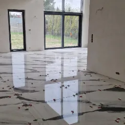 Układanie płytek podłogowych z użyciem klipsów poziomujących w przestronnym, surowym wnętrzu z dużymi oknami.