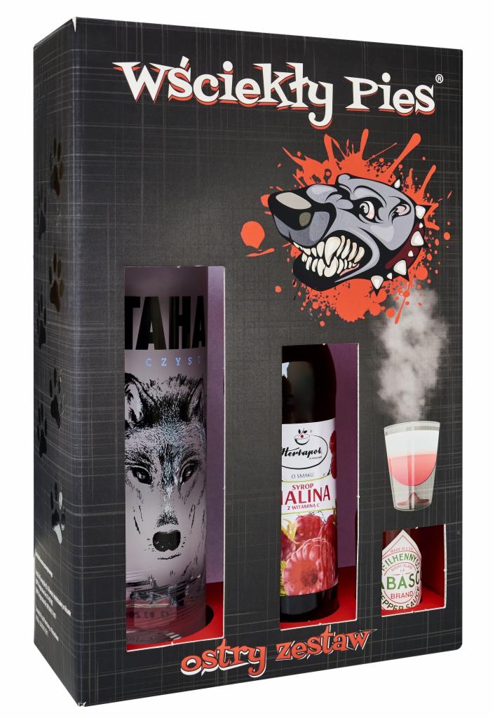 Zestaw prezentowy 'Wściekły Pies' w czarnym pudełku z grafiką wilka, zawierający butelkę wódki z wizerunkiem wilka, syrop malinowy Herbapol i małą butelkę sosu Tabasco, obok drink z parą.