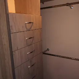 Wnętrze garderoby z szufladami o drewnianym wzorze i chromowanymi uchwytami, widoczne drążki na ubrania.