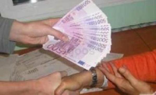 Dwie osoby wymieniają się plikiem banknotów 500 euro na drewnianym stole, widoczny częściowo wypełniony formularz.