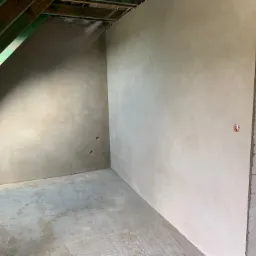 Wnętrze poddasza po nałożeniu gładzi gipsowej, widoczne otwory pod gniazdka elektryczne i surowa konstrukcja dachu.