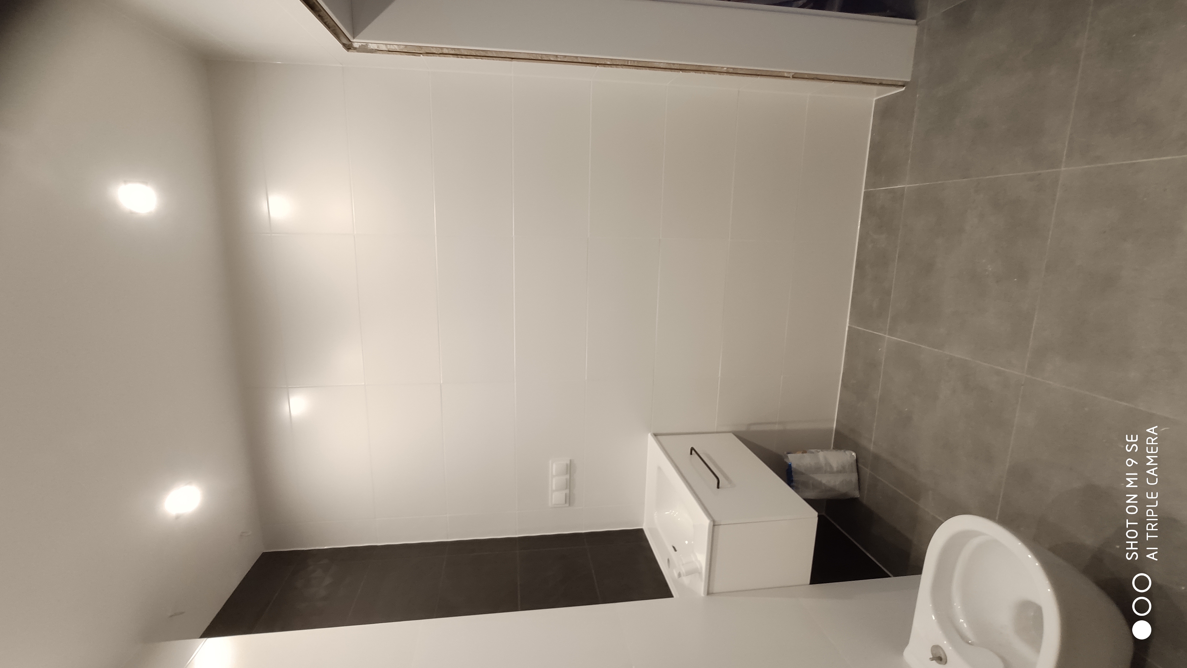 Nowoczesna, jasna łazienka po remoncie w Nadolicach Wielkich: białe płytki ścienne, ciemnoszara podłoga, podwieszana umywalka z szafką i toaleta.