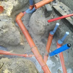 Wykonanie instalacji kanalizacyjnej z rur PCV w wykopie, widoczne połączenia i kształtki, częściowo zalane wodą, z elementami poziomicy w tle.