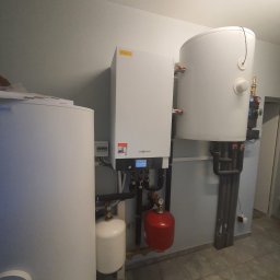 Ecotherm Hydraulik Serwis urządzeń grzewczych Bierutów Oleśnica Jelcz-Laskowice - Zestaw instalacji grzewczej z kotłem, zasobnikiem ciepłej wody i naczyniami przeponowymi w pomieszczeniu technicznym z szarą podłogą.
