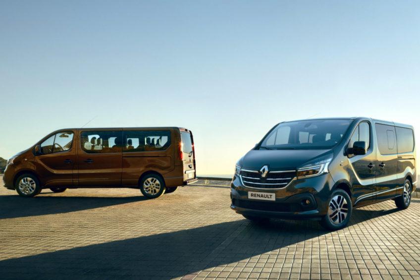 Dwa busy Renault Trafic: ciemnoszary z przodu i brązowy z tyłu, zaparkowane na tle jasnego nieba.