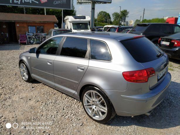 Szary samochód typu kombi marki Audi A3, zaparkowany na żwirowym placu, widok z boku i tyłu, z widocznymi felgami aluminiowymi i tablicą rejestracyjną.