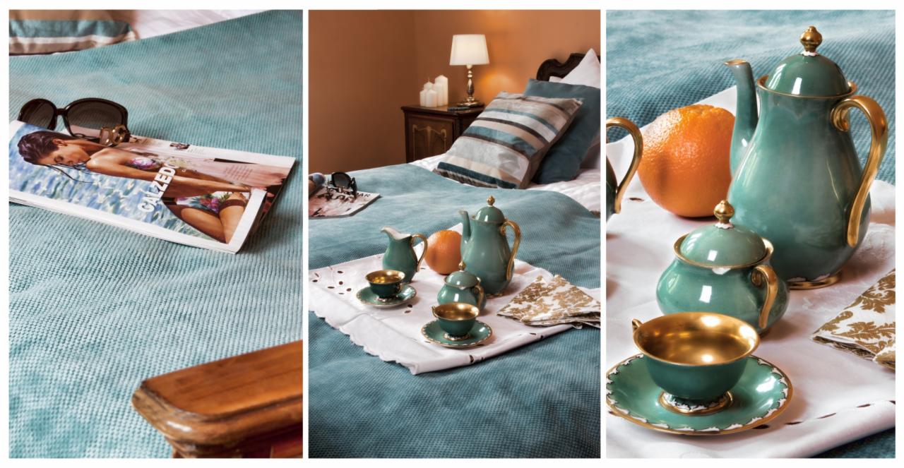 Turkusowa pościel z gazetą, okularami i serwisem do herbaty w złotych zdobieniach na białej tacy z haftem.