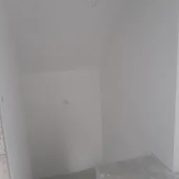 Wnętrze w trakcie prac wykończeniowych: gładkie, białe ściany, szary betonowy podkład, zwisające przewody elektryczne.