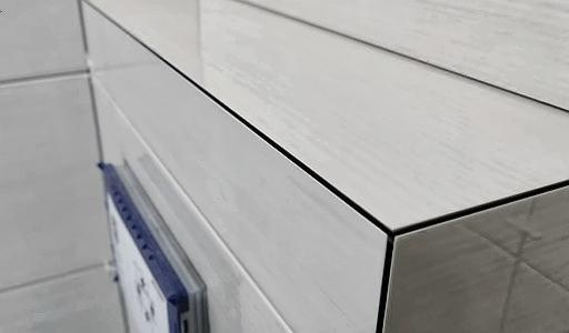 Fragment wykończonej ściany i szafki z błyszczących, białych płytek ceramicznych z widocznymi fugami, z kalendarzem przymocowanym do ściany.