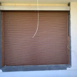 Brązowa roleta zewnętrzna zamontowana w oknie budynku w trakcie ocieplania. Widoczna drabina oparta o ścianę. Kabel zwisający z góry.