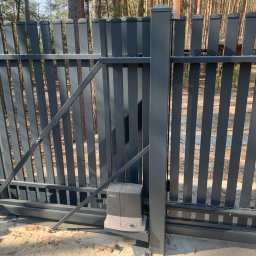 PHU SUN-TEL - Nowoczesna, przesuwna brama wjazdowa w kolorze grafitowym z automatyką Beninca, na tle leśnego krajobrazu. Widoczny napęd bramy i pionowe profile bramy.
