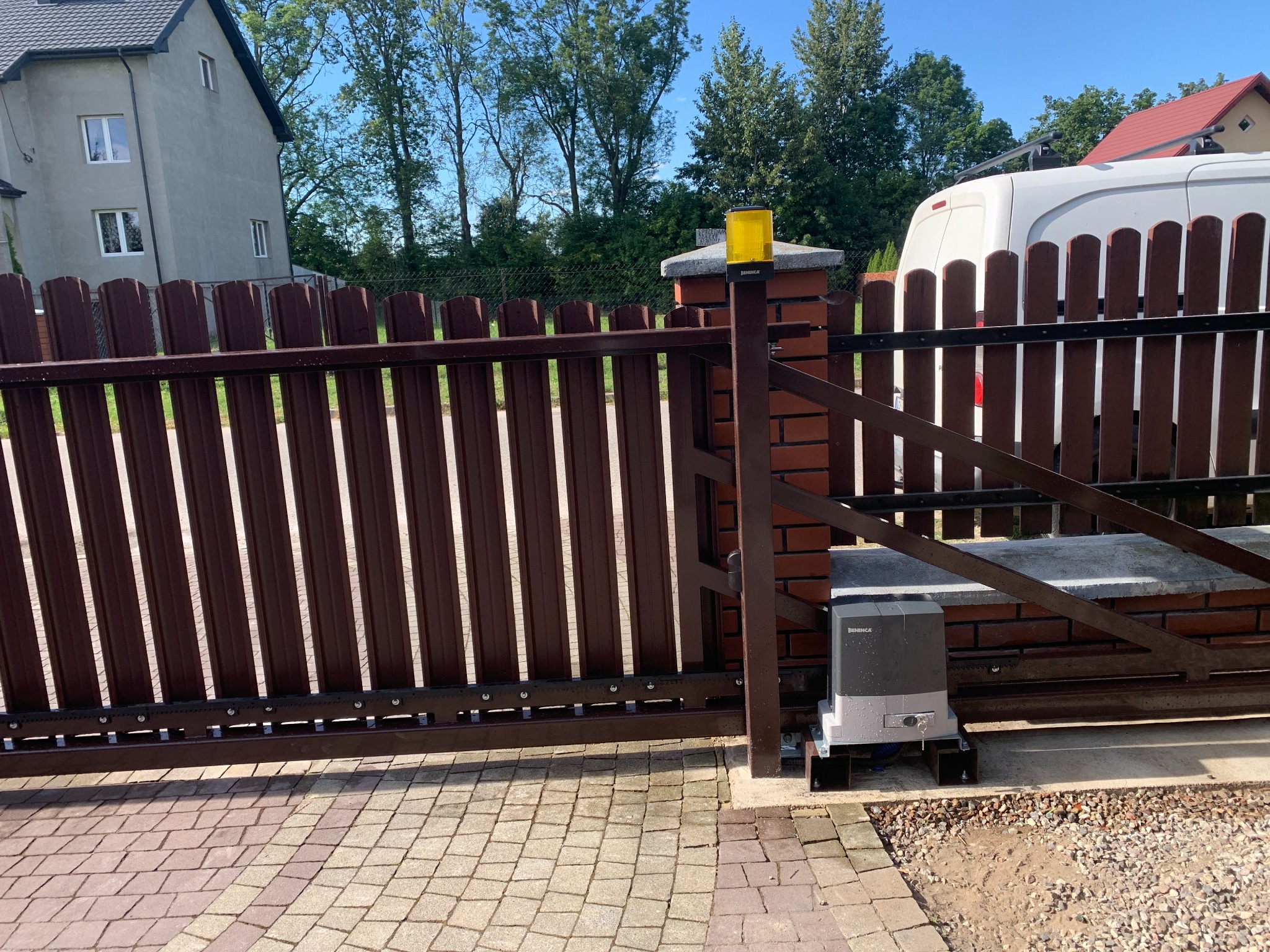 Automatyczna brama przesuwna z brązowymi sztachetami i ceglanym słupkiem, widoczny napęd Beninca. Realizacja w Pułtusku.