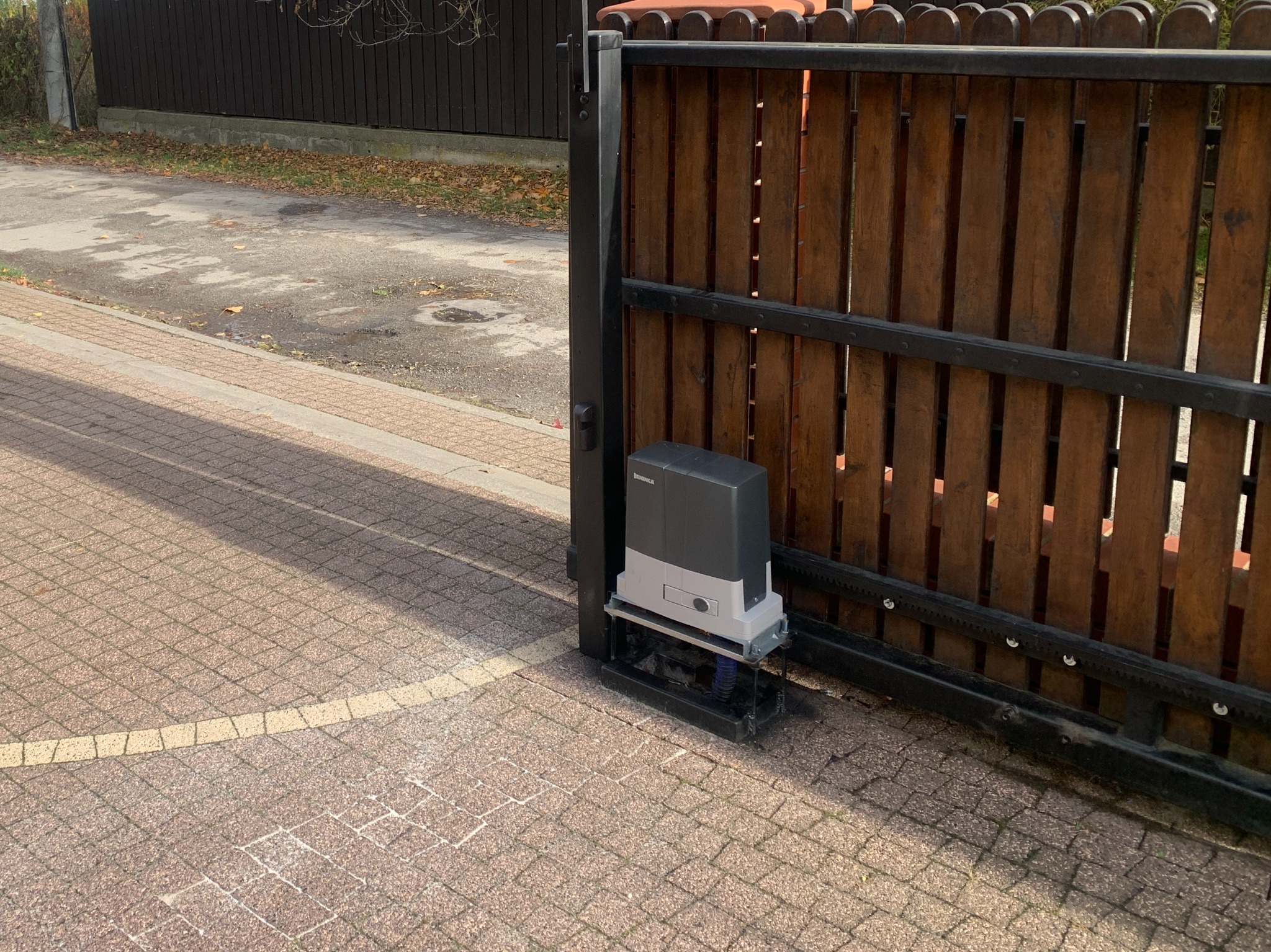 Drewniana brama wjazdowa z automatyką BFT w Pułtusku. Widoczny napęd bramy zamontowany przy słupku. Kostka brukowa na podjeździe.