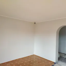 Wnętrze pokoju po odświeżeniu ścian na jasny kolor, widoczny fragment parkietu, drabina w przejściu z łukiem i zabezpieczona podłoga folią malarską.