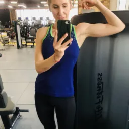 Kobieta w sportowym stroju, robiąca selfie w siłowni, demonstrująca napięte bicepsy