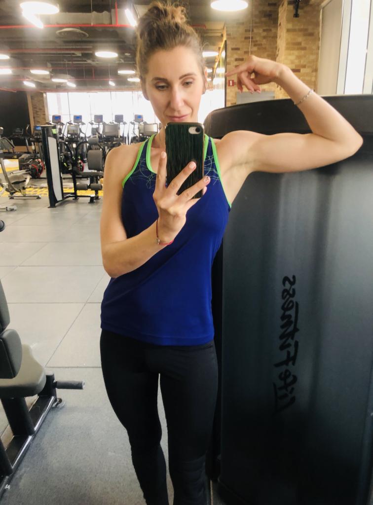 Kobieta w sportowym stroju, robiąca selfie w siłowni, demonstrująca napięte bicepsy