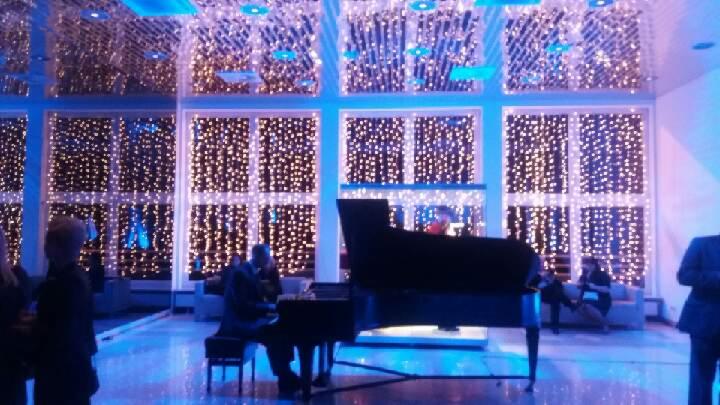 Pianista gra na fortepianie w przestronnym wnętrzu z oknami udekorowanymi girlandami świetlnymi, tworząc elegancką atmosferę.