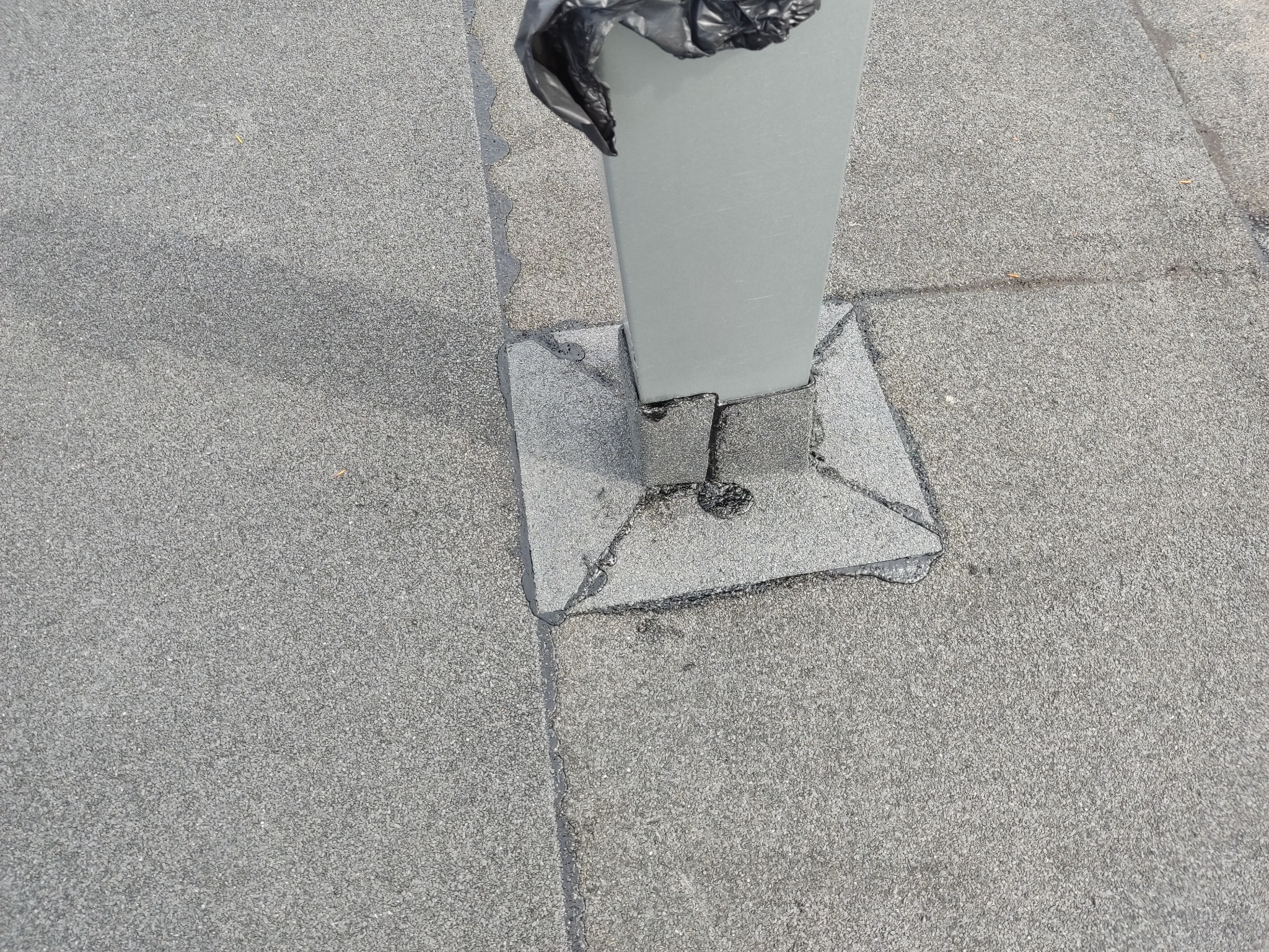 Szary, płaski dach pokryty papą z widocznym słupkiem zabezpieczonym czarną folią, uszczelnionym wokół podstawy.