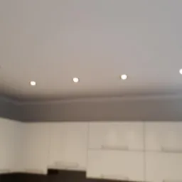 Biały sufit z rzędem sześciu punktowych lamp halogenowych w nowocześnie urządzonej kuchni z białymi szafkami.