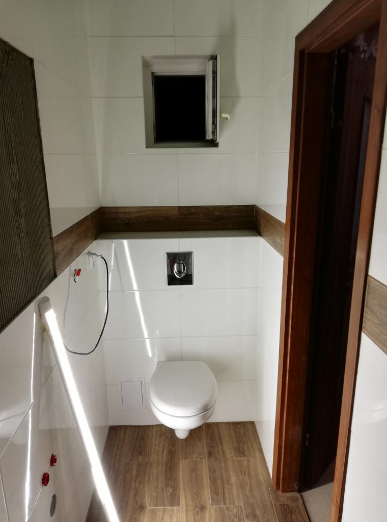 Wykończona łazienka z wiszącą toaletą, białymi płytkami i drewnopodobną podłogą oraz obramowaniem, okno z otwartym skrzydłem.