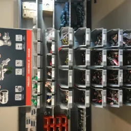 Regał z szufladami zawierającymi złączki hydrauliczne i zawory, obok plansza reklamowa Calido prezentująca produkty.