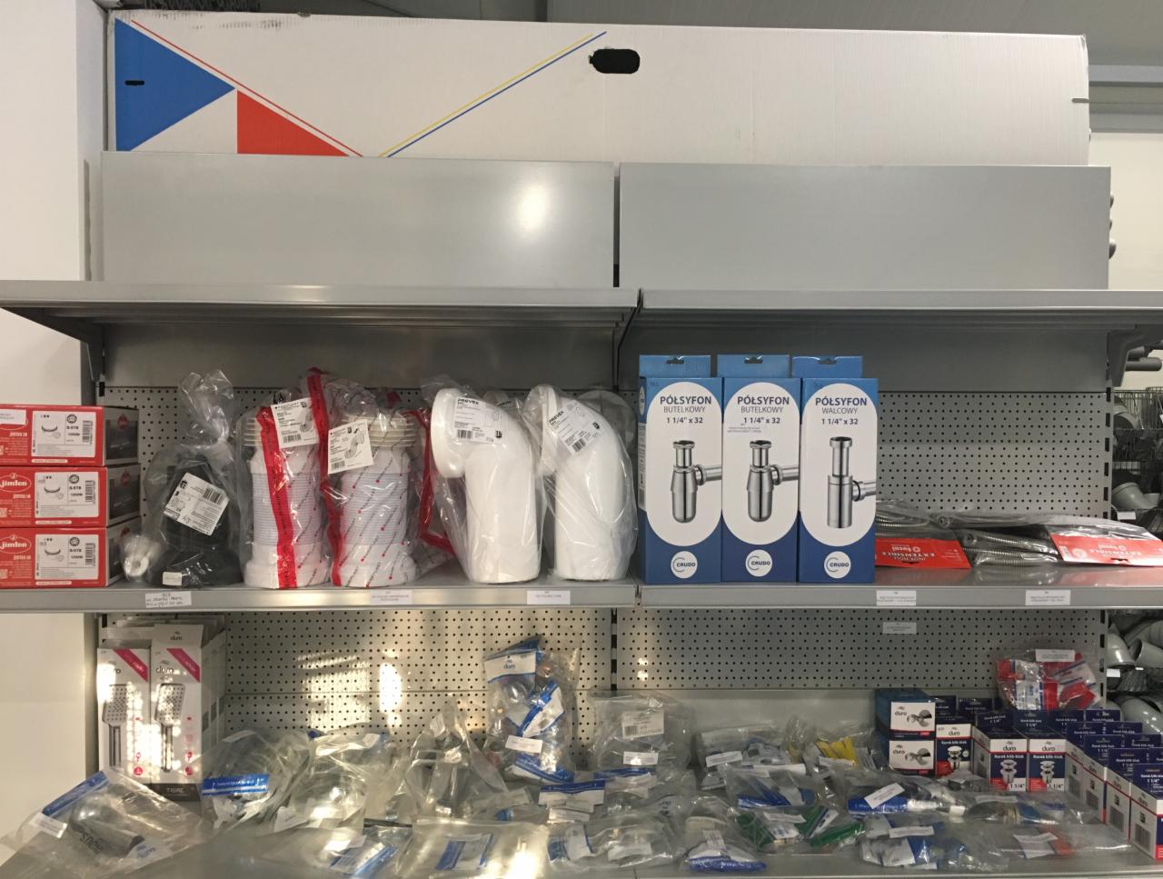 Półki w sklepie instalacyjnym w Iwkowej, na których znajdują się różnego rodzaju syfony, złączki i inne elementy instalacyjne, w tym opakowania z syfonami butelkowymi i walcowymi.