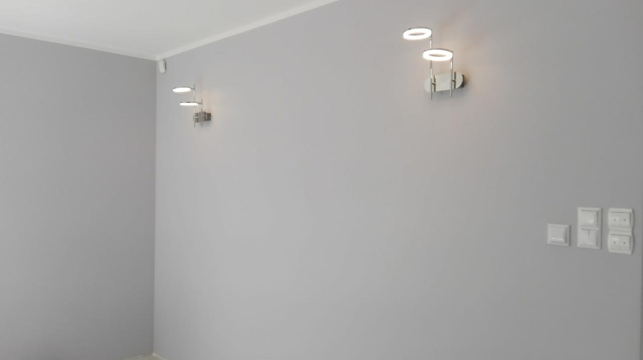 Jasnoszara ściana w pokoju z zamontowanymi nowoczesnymi, podwójnymi lampami LED i białymi włącznikami światła.