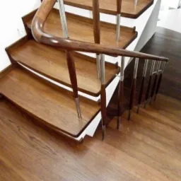 Drewniane schody z poręczą z ciemnego drewna i metalowymi wspornikami, widok z góry na stopnie z wyraźnym rysunkiem słojów.