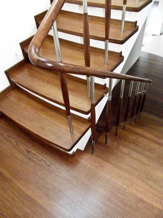 Drewniane schody z poręczą z ciemnego drewna i metalowymi wspornikami, widok z góry na stopnie z wyraźnym rysunkiem słojów.