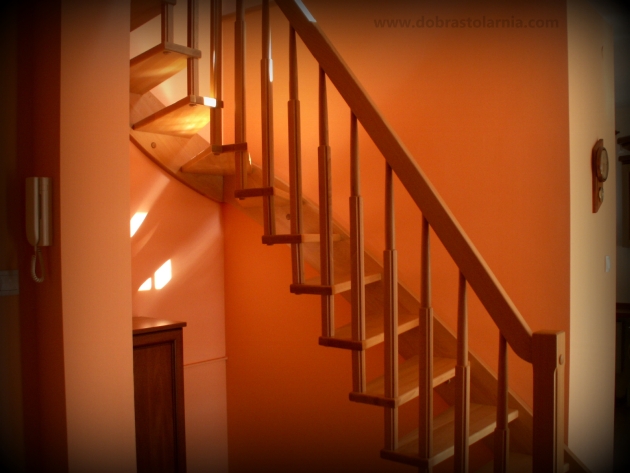Drewniane schody z jasnego drewna na pomarańczowej ścianie, oświetlone promieniami słońca wpadającymi przez okno.