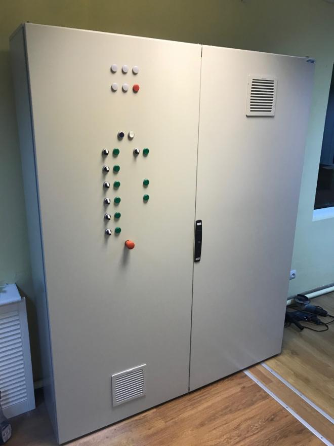 Duża, dwudrzwiowa szafa sterownicza z przyciskami i kratkami wentylacyjnymi, widoczne narzędzia na podłodze