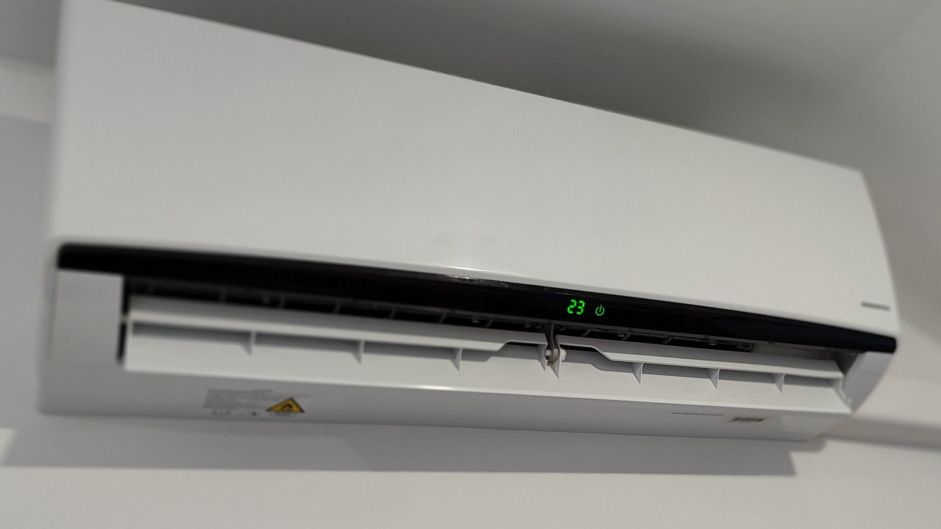 Biała, naścienna jednostka wewnętrzna klimatyzacji z wyświetlaczem pokazującym temperaturę 23 stopnie Celsjusza, zamontowana na jasnej ścianie.